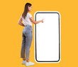 © Prostock-studio - Full Body Length Back View Of Woman Using Big Smartphone With Blank White Screen And Touching Display Panel With Finger, Cheerful Lady Standing On Yellow Background, Ordering Food Delivery, Mock Up