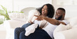 © Prostock-studio - A couple is laughing and pointing at something off-screen while relaxing on a white couch in their living room.