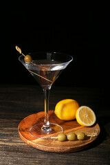 Wall Mural - Glass of tasty martini, lemons and olives on wooden table against dark background