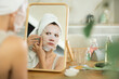 © JackF - Serene woman with towel head wrap looking in mirror and gently placing cosmetic face mask on, enjoying moment of tranquility and self-care ..
