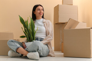 Poster - Pretty young woman with houseplant and cardboard boxes in new apartment. Moving house concept