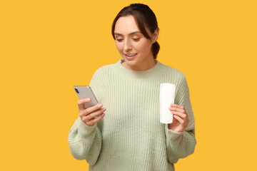 Wall Mural - Beautiful young woman with menstrual pad and mobile phone on yellow background