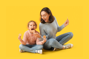 Sticker - Young mother and her little daughter eating tasty cookies on yellow background