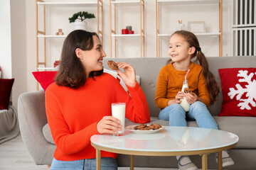 Poster - Young mother and her little daughter eating cookies with milk at home