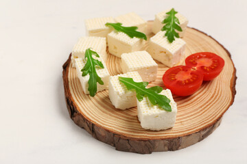 Wall Mural - Wooden board with delicious feta cheese pieces, tomatoes and arugula on white grunge background