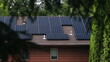 © Tyler - Solar photovoltaic panels on the roof of a red house framed by a foreground of green trees. Solar Panel Module technology creating renewable energy in New Jersey.