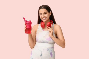 Poster - Beautiful young happy woman with headphones and sports bottle of water on pink background