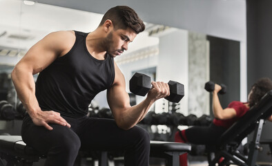 Wall Mural - Arab muscular man doing biceps workouts with dumbbells in gym, copy space