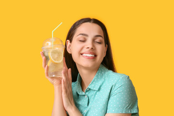 Canvas Print - Beautiful young happy woman with cup of fresh lemonade on yellow background