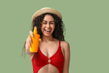 Wall Mural - Beautiful young happy African-American woman with bottle of sunscreen cream on green background