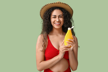 Wall Mural - Beautiful young happy African-American woman with bottle of sunscreen cream on green background