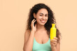 © Pixel-Shot - Beautiful young happy African-American woman with bottle of sunscreen cream on beige background