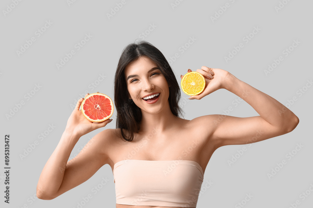 Beautiful young woman with grapefruit and orange on grey background