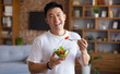 © Prostock-studio - Happy asian mature man holding fork and bowl with fresh vegetable salad, eating healthy lunch after domestic training. Active middle aged male having balanced meal