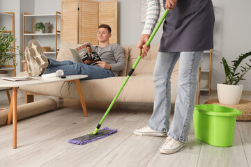 Canvas Print - Lazy husband reading magazine while his wife mopping at home