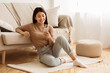 © Prostock-studio - Happy Asian Girl Messaging on Phone at Home, Sitting on Floor near Sofa