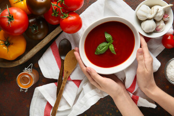 Wall Mural - Female hands with bowl of fresh tomato soup and garlic on dark background