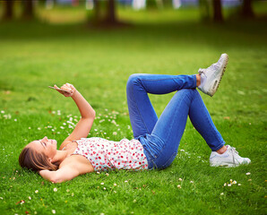 Wall Mural - Woman, phone and lying on lawn with reading, texting and smile for notification, chat and contact in spring. Girl, student and happy with smartphone on grass at campus to relax, click or social media