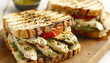 © ЮРИЙ ПОЗДНИКОВ - A delicious grilled chicken sandwich with pesto and tomatoes presented on a wooden cutting board