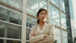 © Chatchanan - Confident woman in a beige suit, arms crossed, standing in front of a modern building