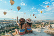 © mister - Two friends sitting on the top of hill, overlooking hot air balloons