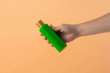 Wall Mural - Green shampoo bottle in hand isolated on cream background