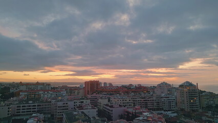 Cloudy coastal city sunset drone view. Town at ocean coast evening sun light