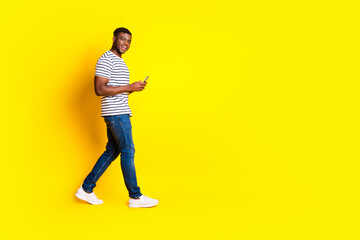 full body portrait of nice young man walk empty space phone wear t-shirt isolated on vibrant yellow 