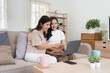 © itchaznong - Happy Mom and Daughter Bonding at Home, Smiling and Using Laptop Together in Cozy Living Room