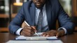 © Daniel - Horizontal closeup image black businessman sitting at desk and signing contract