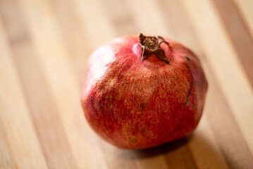 Wall Mural - One red pomegranate on a wooden table, close up. Juicy pomegranate laying on striped wooden surface, lightened with sunshine