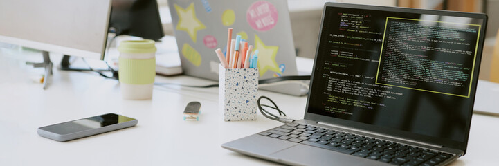 Website header shot of laptop surrounded with phone and office supplies on white wooden table