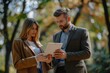 © vefimov - Man and woman discussing work on tablet in sunny park setting.