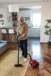 © Jelena Stanojkovic - Bearded senior man cleaning carpet with vacuum cleaner at home. Senior man vacuum cleaning home.