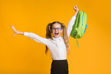 Wall Mural - Happy Schoolgirl Enjoying School Break Playing With Backpack On Yellow Background. Free Space