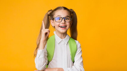 Wall Mural - Idea Concept. Excited Primary School Girl Pointing Finger Up Over Yellow Studio Background. Empty Space