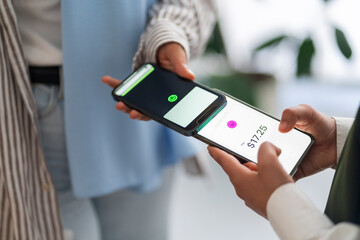 Close-up of two people using their mobile phones for tap to pay contactless payment One phone displays the amount to be paid, showing a modern and convenient transaction method