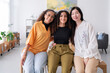 © Studio Marmellata - Three diverse women smile together in a bright modern office The women are dressed in colorful outfits and are standing close to each other showcasing their camaraderie and friendship