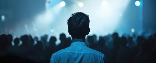 Wall Mural - A man in the foreground facing away from the camera, a crowd of people surrounding him, with light blue and white lighting in a night time concert atmosphere.