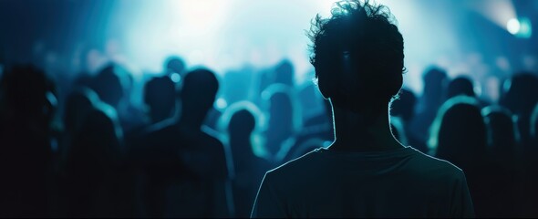 Wall Mural - A man in the foreground facing away from the camera, a crowd of people surrounding him, with light blue and white lighting in a night time concert atmosphere.