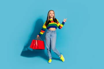 Poster - Full body photo of attractive young woman shopping bags point empty space dressed stylish striped clothes isolated on blue color background