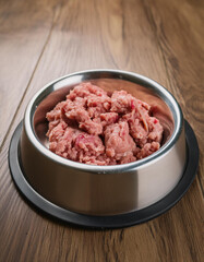 Stainless steel pet bowl with raw ground turkey on wooden floor. Healthy dog food.