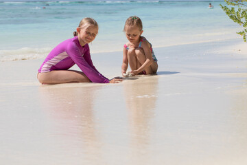 children playing on the ocean shore in the sand, sand castle, sisters, white sand, blue ocean, exotic vacation