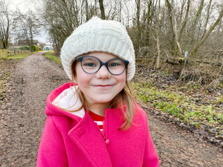 Portrait of a cute school girl with eyeglasses outdoors in park. Happy funny child on autumn, spring or winter day.