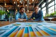 © YURY YUTY - Two professionals in a modern office, discussing data charts and graphs on a table.