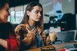 © BullRun - Two charming hipster girls enjoying coffee break waiting webinar online on laptop computer connected to cafeteria wifi, young beautiful female students preparing for university test together