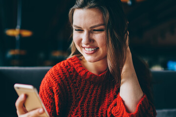 Wall Mural - Prosperous millennial hipster girl chatting with friends in break of blogging using 4g internet indoors, happy cheerful woman reading email from colleague connected to wireless at college cafeteria