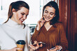 © BullRun - Cheerful female bloggers sharing information via bluetooth connection on smartphones, positive smiling women enjoying time together chatting with followers via mobile phones resting at coffee shop