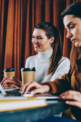 Wall Mural - smiling hipster girl watching funny videos while female friend near waiting important webinar on lap
