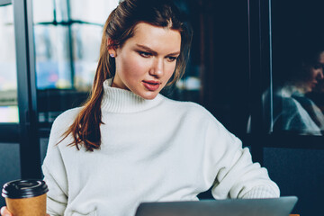 Wall Mural - Serious female software developer creating web page typing program code using laptop device for work, caucasian woman holding takeaway coffee and watching important webinar learning computer service